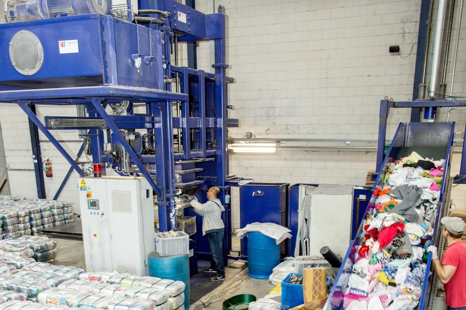 Kledingstukken van de sorteerband worden verpakt in grote textielpakketten.