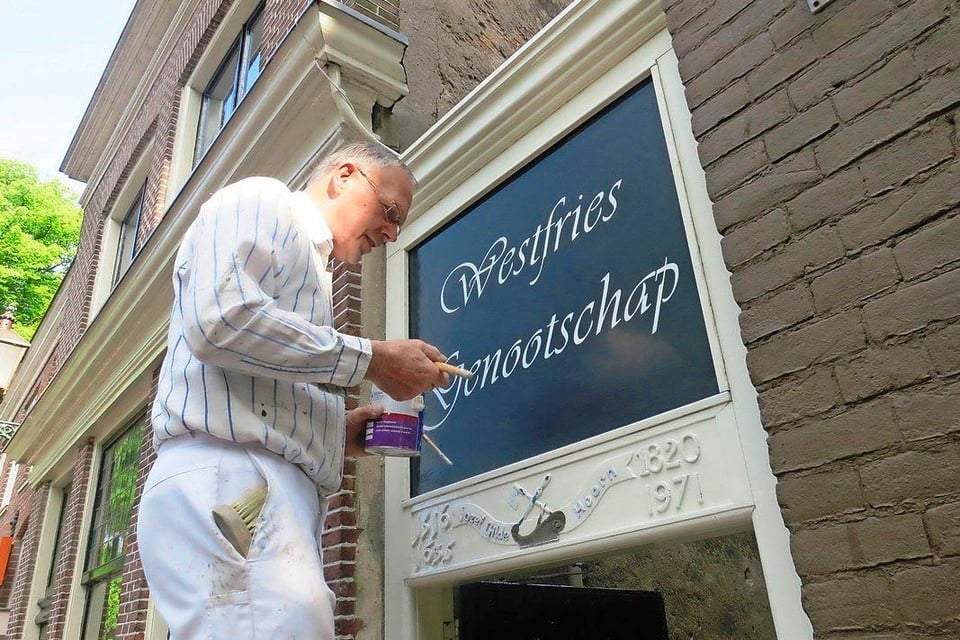 Bestuurslid Hans van Kampen van het Westfries Genootschap (Hoorn) schildert de verenigingsnaam op het toegangspoortje van het Timmermansgildehuisje.