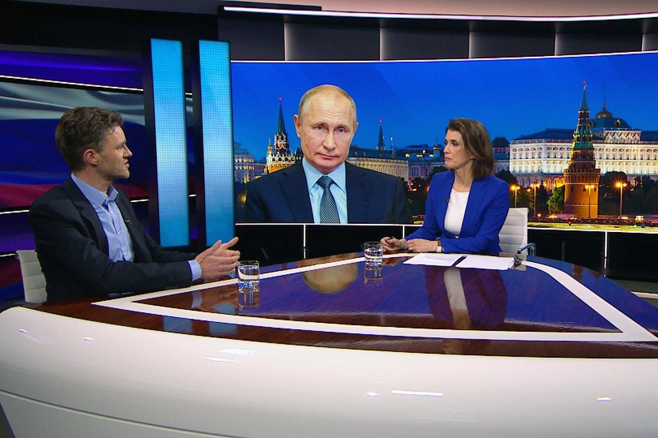Bob Deen in gesprek met Mariëlle Tweebeke, tijdens een uitzending van Nieuwsuur. Op het scherm president Putin.