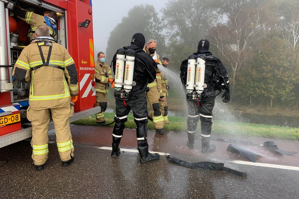 De actie is voorbij en de prut op de pakken van de twee brandweerduikers wordt met een brandslang weg gespoten.