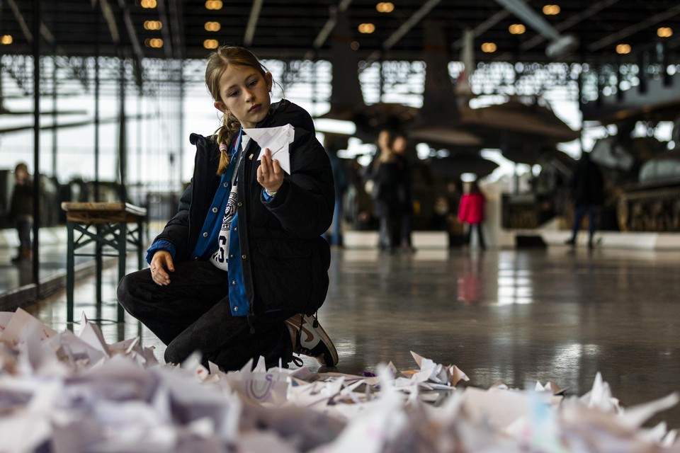 Een meisje leest teksten op de vele honderden gevouwen vredesduifjes in het Nationaal Militair Museum.