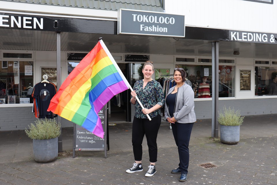 Wethouder Rabella Wiersma-de Faria( rechts) reikt de regenboogvlag uit aan Tokoloco Fashion in Spanbroek.