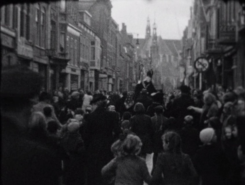 De optocht door de Langestraat. Hoog boven al het publiek de Sint (op zijn rug gezien). Zwarte Piet had het heel druk met uitdelen van lekkers.