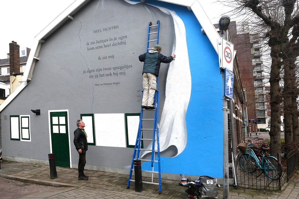 Eric van der Vegt is bezig met de muurschildering rond het gedicht. Dichter Jeroen Paulussen kijkt toe.