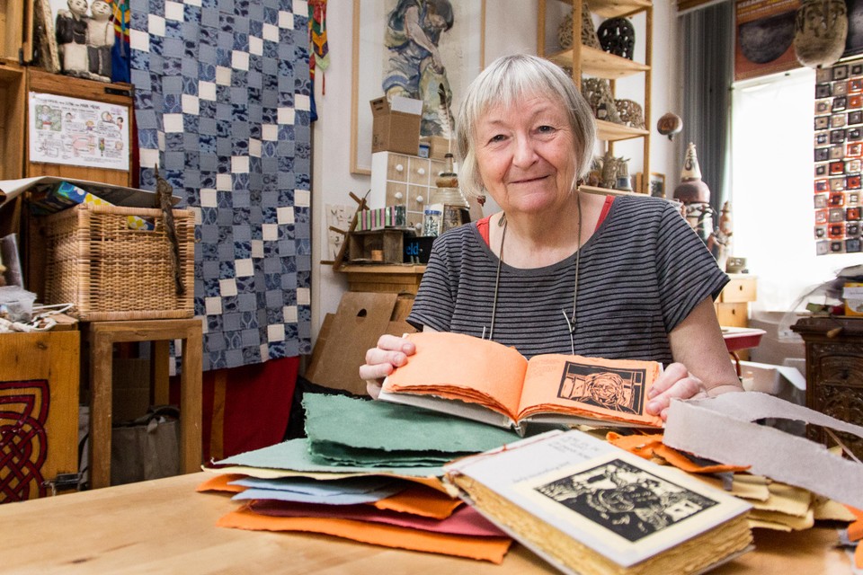 Berty Sieverding in haar atelier met een tafel vol papier en de twee door haar gemaakte boekjes van Zaansch Bord. Aan de muur en voor het raam de papieren wandkleden.